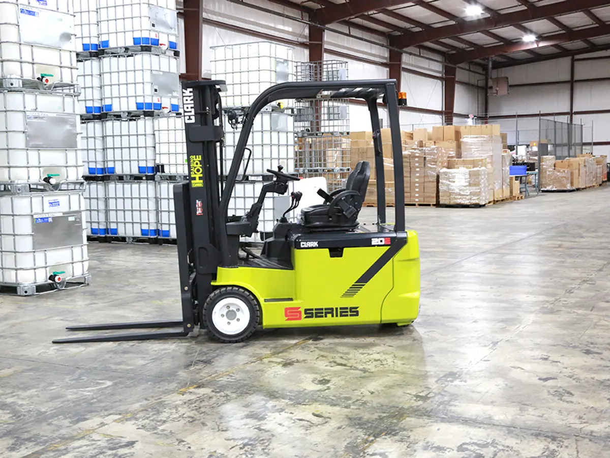 Clark electric forklift on a warehouse floor beside stacked totes and cartons